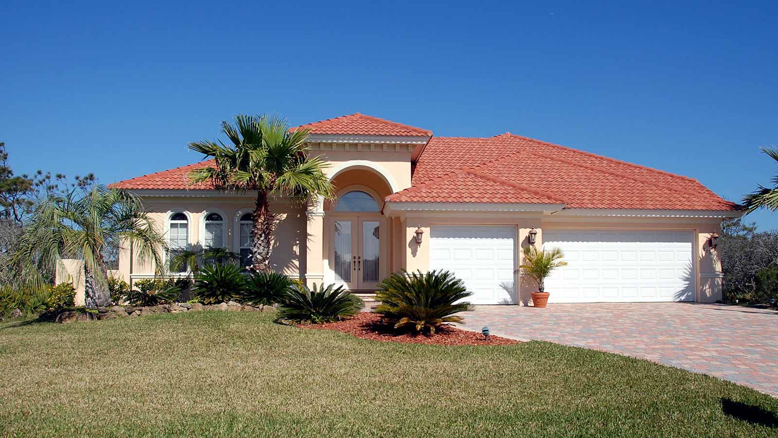 Front view of a single-story home with a red tile roof, arched entryway, and attached three-car garage under a blue sky