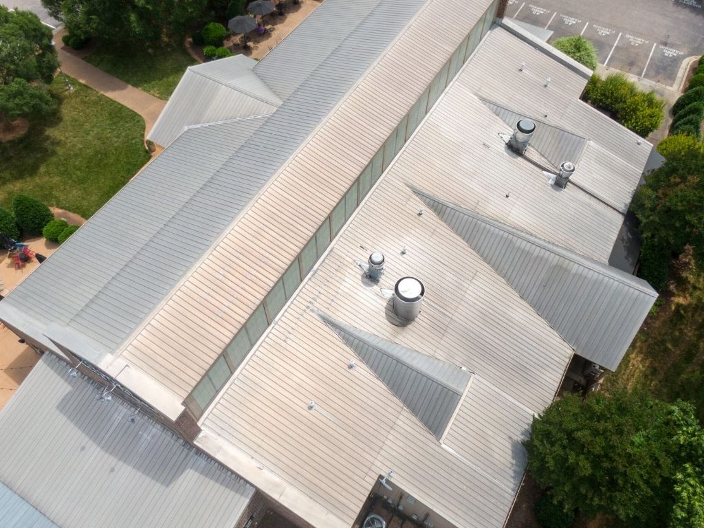 Aerial view of a commercial building with a metal roof, featuring several vents and a clean, well-maintained surface. The roof demonstrates the durability and longevity of metal roofing systems in commercial applications.
