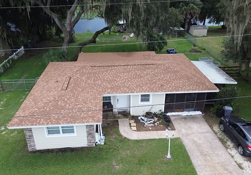 Aerial drone view of a Florida single-family home with a newly installed tan asphalt shingle roof, showing multiple roof planes, covered porch, driveway, and surrounding yard.