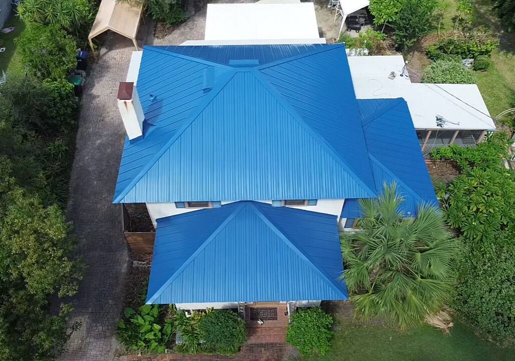 Top-down drone view of a Florida residential home with a newly installed blue metal roof, showing multiple roof planes, ridgelines, and surrounding landscaping.