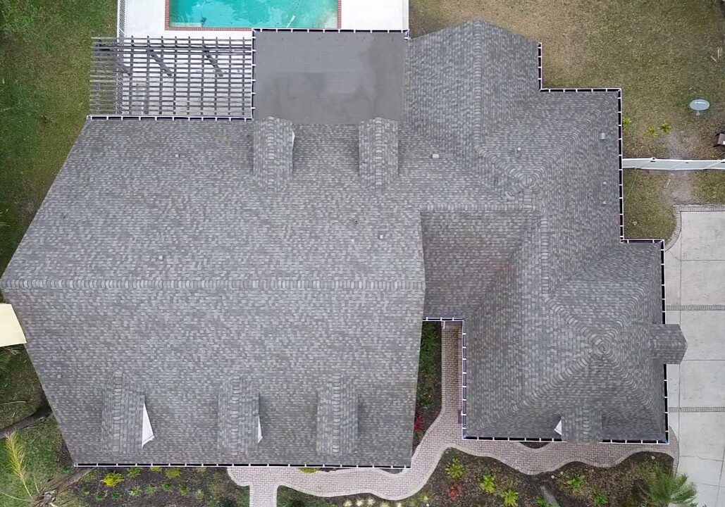 Top-down drone view of a Florida residential home with a newly installed light gray asphalt shingle roof, showing multiple roof planes, ridgelines, vents, driveway, and screened backyard pool.