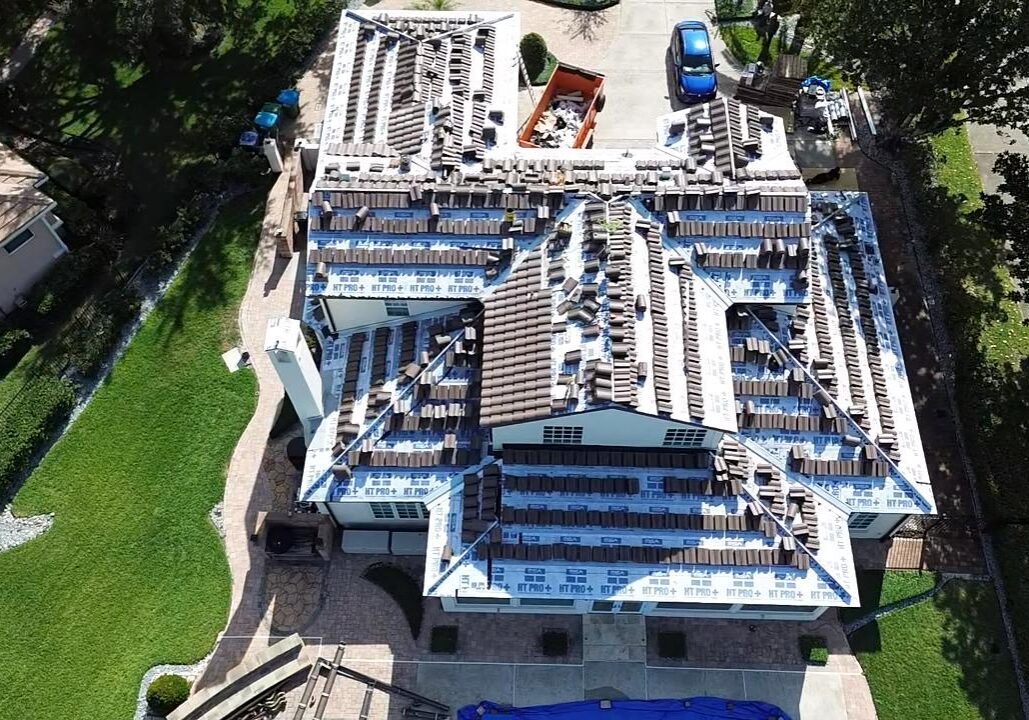 Top-down drone view of a Florida residential home during roof replacement, showing underlayment installation, stacked roof tiles, and active roofing work in progress.