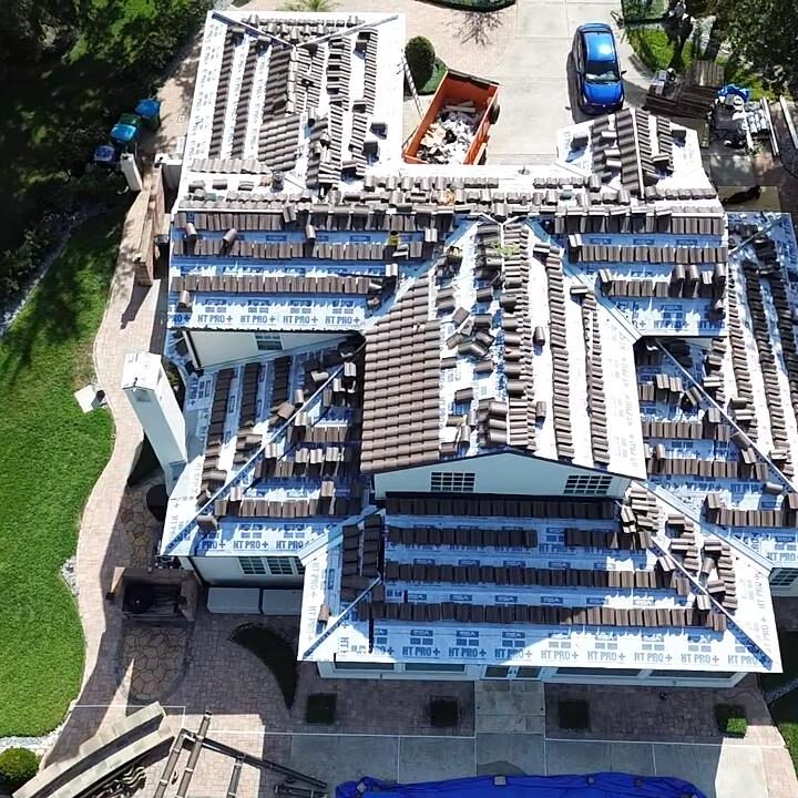 Top-down drone view of a Florida residential home during roof replacement, showing underlayment installation, stacked roof tiles, and active roofing work in progress.